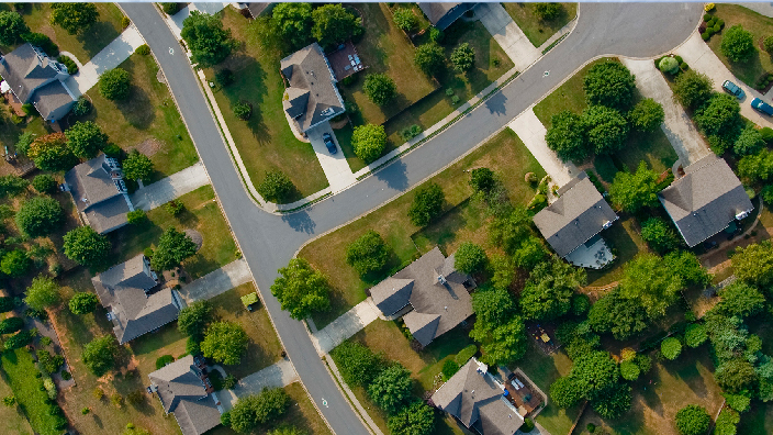 Aerial view of a suburban neighborhood dotted with tidy pale-roofed houses and bright green trees