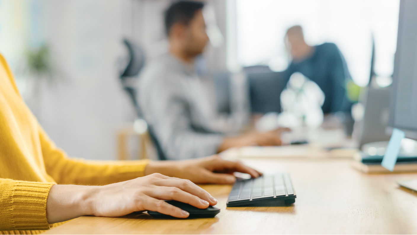 Person with a yellow sweater using a keyboard and a mouse sitting at a desk