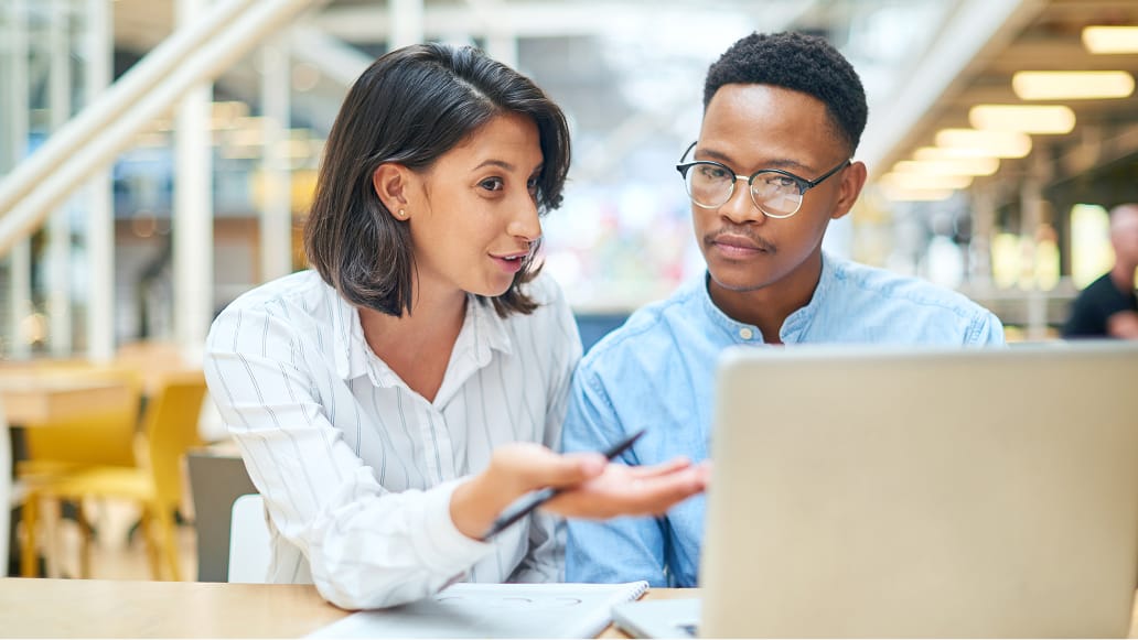 Two business professionals sitting at a conference table discussing a shared laptop display in a bright modern office setting