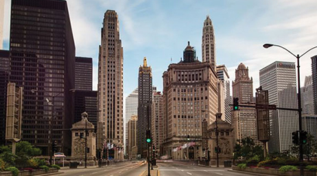 A street-level view of a major city with historic skyscrapers beneath a hazy blue sky