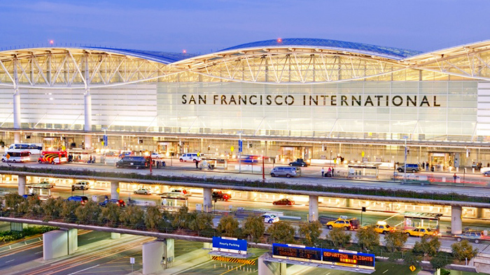 The front curbside of the San Francisco International Airport lined with many cars passing through beneath a hazy blue evening sky