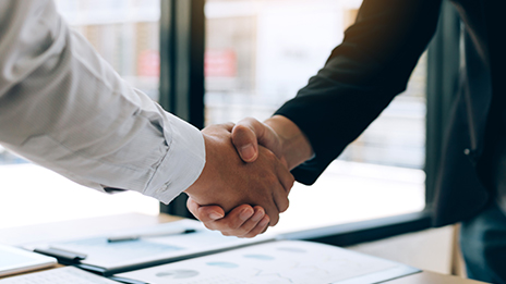 A close-up photo of two hands clasped in a handshake over a conference table