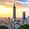 A city skyline showing tall buildings and a blue sky with mountain peaks in the background