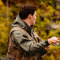 A young person wearing a camouflage vest, fishing in a forest