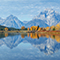 A panorama view of a still river reflecting the sky bordered by yellow autumn trees with a wide blue mountain range in the background 