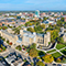 Aerial view of a tree-filled university campus with historic stone and brick buildings and a sprawling city in the distance