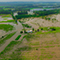 An aerial image of a white farmhouse and adjacent buildings beside wide green crop fields, all deeply flooded with still brown flood water