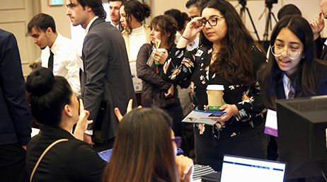 A crowded room in a convention center with many young professionals mingling as they check in at the registration desk
