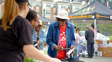 A photo of three casually dressed people talking and laughing at an outdoor food bank event with awnings and boxes in the background