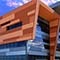 A modern building in mirrored blue glass and brown paneling under a cloud-streaked vivid blue sky