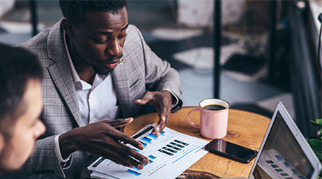 Two professionally-dressed people sharing a desk discussing a page full of graphs and data in a modern office