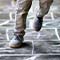 A pair of child’s feet wearing brown shoes and khaki pants jumping on a chalk hopscotch pattern