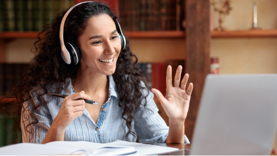 A person sitting at a desk wearing headphones talking animatedly at a person through a computer