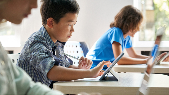 Children sitting at desks and working on individual tables in a light-filled room 