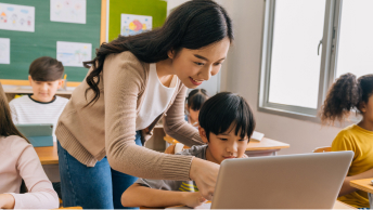 A teacher helping a young student sitting at a desk with a computer