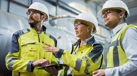 Three heavy industry engineers standing  in a factory, using a tablet and discussing design