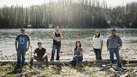 Small group of men and women standing near a river and a forest
